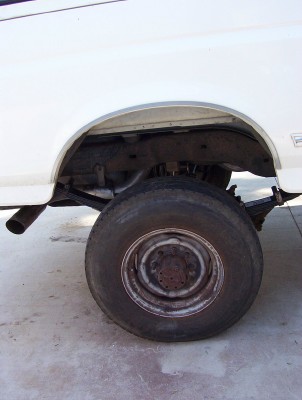 1995 Ford Bronco - Close-up of the rear wheel and suspension system of a white SUV, with visible rust on the frame components.