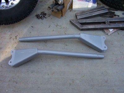 1995 Ford Bronco - Two suspension control arms are laid out on a concrete surface with various metal parts and a tire nearby.