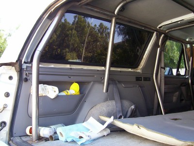 1995 Ford Bronco - The interior of the vehicle features a full roll cage, custom modifications, and items stored in the rear compartment.