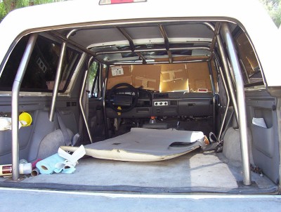 1995 Ford Bronco - The interior of a modified Ford Bronco shows a roll cage and a partially removed carpet, with cardboard taped to the rear window.