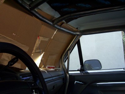 1995 Ford Bronco - The interior of a vehicle shows a roll cage and custom paneling on the windshield.