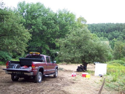 2001 Ford Crown Victoria - A red pickup truck and an ATV are parked in a wooded area with some equipment around.