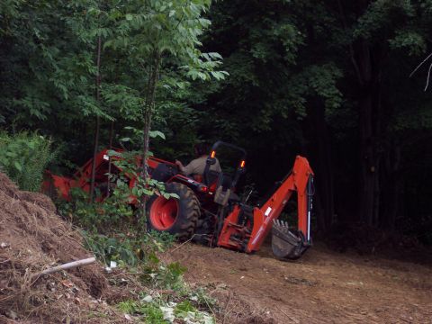 2001 Ford Crown Victoria - A tractor with a backhoe attachment is seen working in a wooded area, with a pile of dirt to the left.