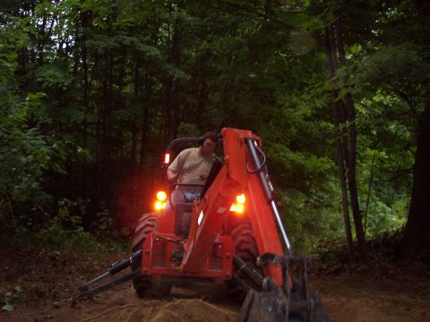 2001 Ford Crown Victoria - A man operates an orange tractor with a front loader in a wooded area.