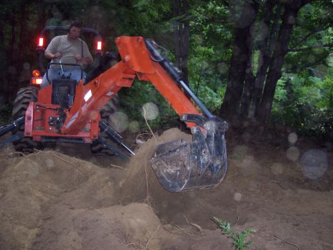 2001 Ford Crown Victoria - A tractor with a backhoe attachment is actively digging into a mound of dirt and exposed roots.