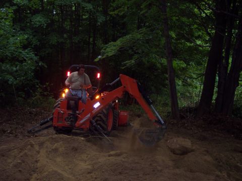 2001 Ford Crown Victoria - Tractor with backhoe digging dirt in a wooded area.