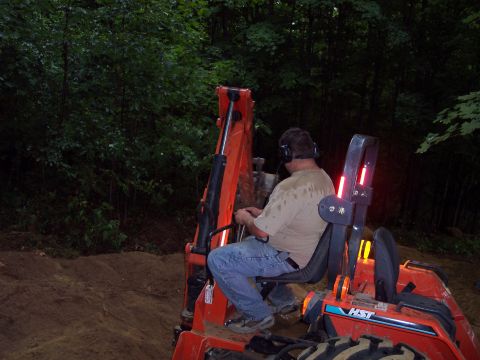 2001 Ford Crown Victoria - Operator controls a backhoe loader in a dirt area surrounded by trees.