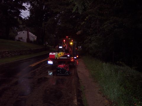 2001 Ford Crown Victoria - A trailer carrying equipment is parked on the side of a wet road at night, with a house visible in the background.