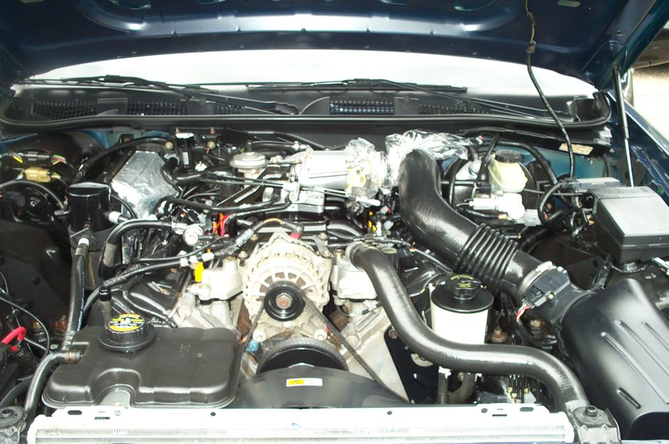 Engine bay of a blue vehicle showing intake, alternator and air intake tube