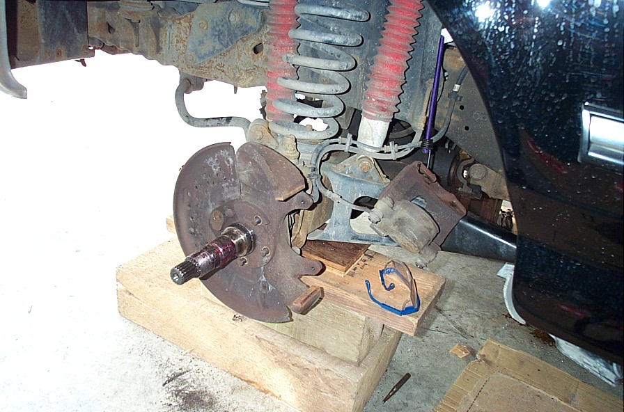 Disassembled front hub on a lifted 4x4 with splined axle shaft exposed, rotor and caliper loose on wood blocks