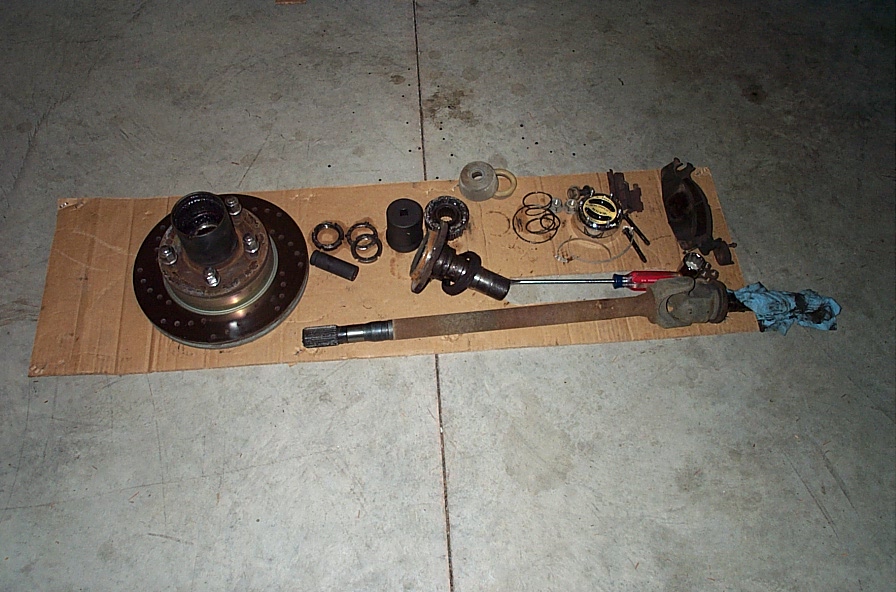 Disassembled front axle parts laid out on cardboard: hub/rotor, spindle, bearings, axle shaft with U-joint, caliper