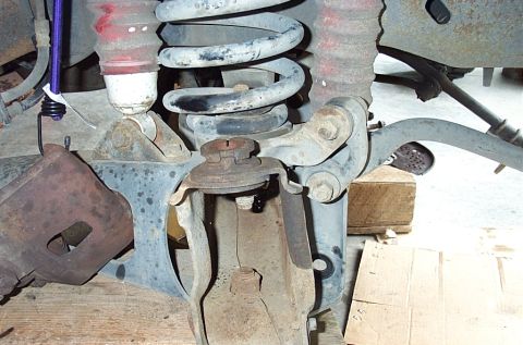 1995 Ford Bronco - Close-up under a truck's front suspension showing the coil spring, red-booted shock absorber, upper and lower ball joints and axle bracket…