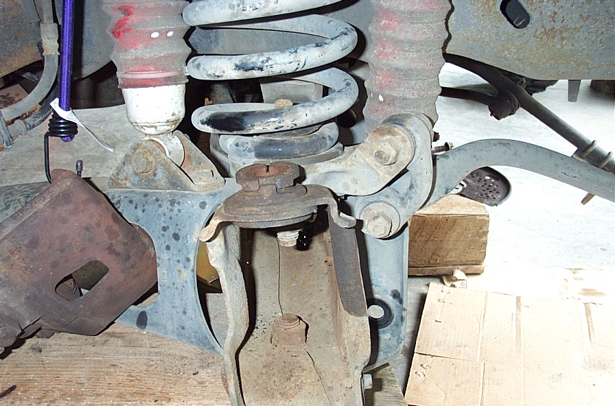 Front coil spring, red shock boot and exposed ball joints with knuckle removed on a lifted truck