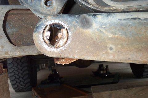 1995 Ford Bronco - Underbody close-up of a rusty suspension link or radius arm eye with the rubber bushing burned/torn out, leaving a hollow ring and a wooden…