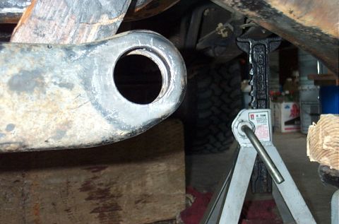 1995 Ford Bronco - Extreme close-up of a radius arm's rear bushing eye, freshly cleaned and bare, resting on a wood cribbing block under a truck. A 6-ton vehi…