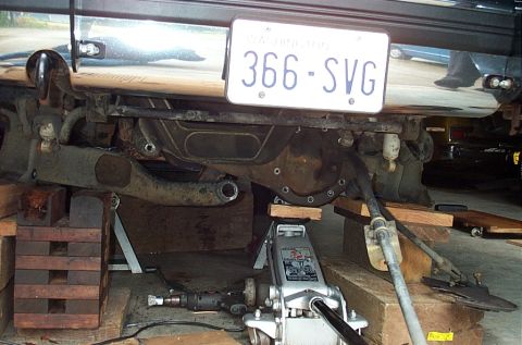 1995 Ford Bronco - Front view under a 4x4 mid-teardown, with the axle housing, radius arms and steering linkage exposed and the truck resting on stacked wood…