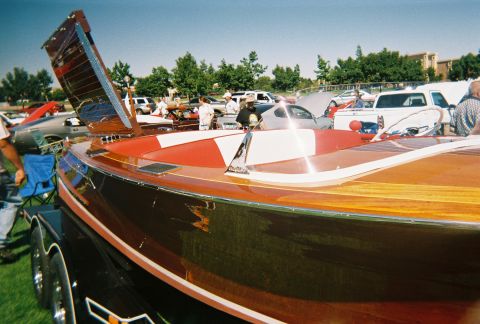 1972 Ford Ranchero - A classic wooden boat is displayed at an outdoor event, with several cars visible behind it.