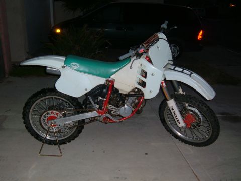 1985 Ford Bronco II - A white dirt bike with a green seat and red frame is parked on a concrete surface.