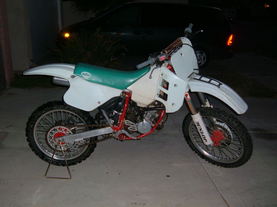 White dirt bike with a green seat and red frame, on a kickstand
