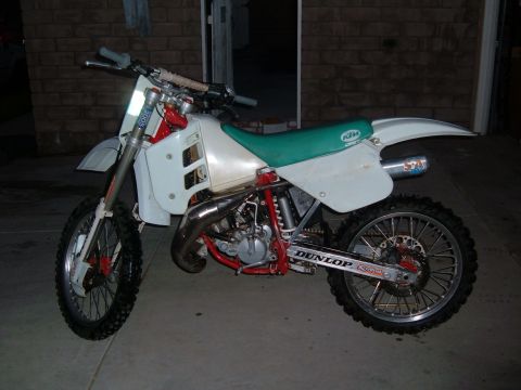 1985 Ford Bronco II - A white dirt bike with a green seat and red frame is parked outdoors.