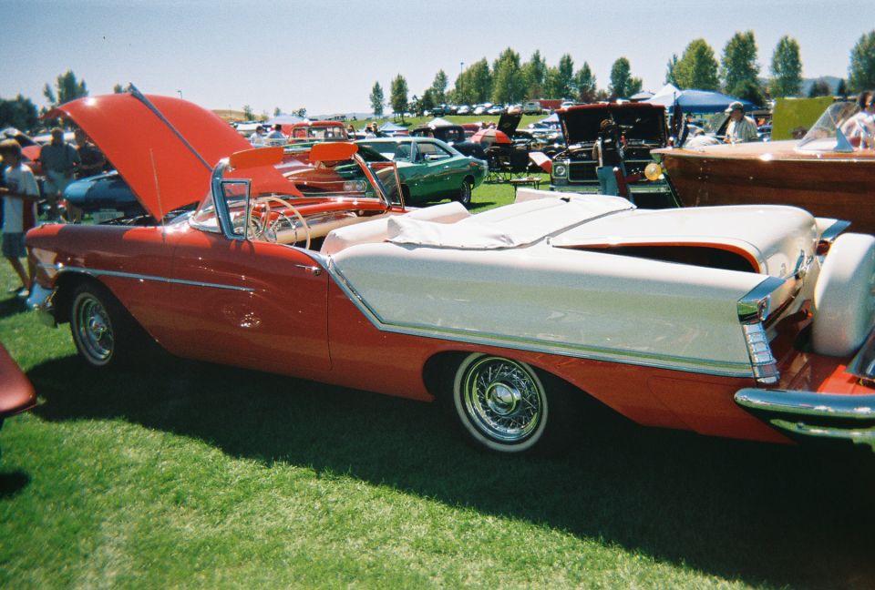 Red and white convertible with hood up, parked on grass at an outdoor car show