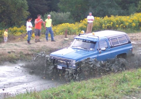 1979 Ford F-150 - A blue SUV navigates a muddy obstacle course, sending mud flying.