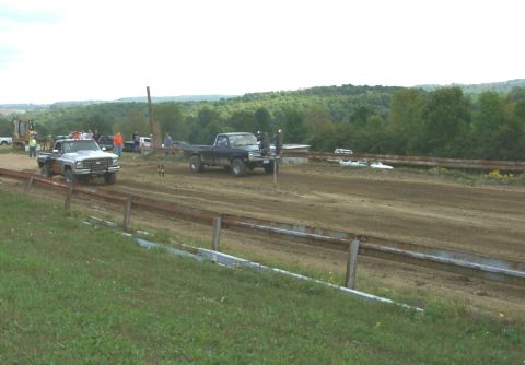 1979 Ford F-150 - Two pickup trucks compete on a dirt track with spectators and trees in the background.