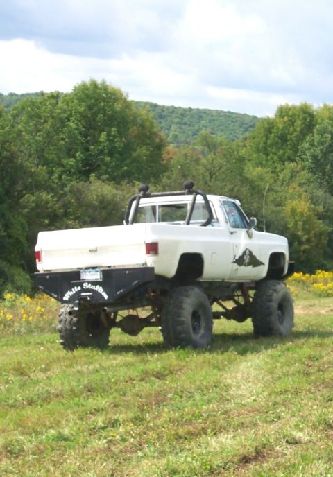 1979 Ford F-150 - This lifted pickup truck is parked in a grassy field with trees and hills in the background.