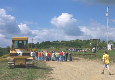 1979 Ford F-150 - A yellow bulldozer is parked on a dirt path with a crowd of people gathered nearby.