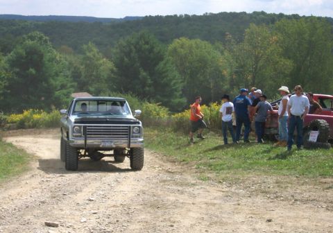 1979 Ford F-150 - A group of people watch as a pickup truck drives down a dusty rural road.