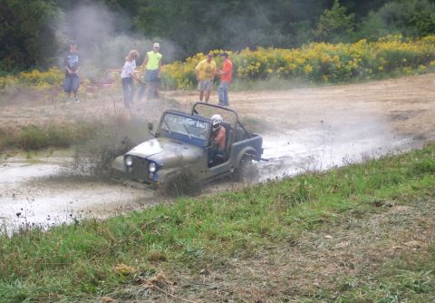 1979 Ford F-150 - A Jeep CJ-7 navigates a muddy off-road course, kicking up spray.