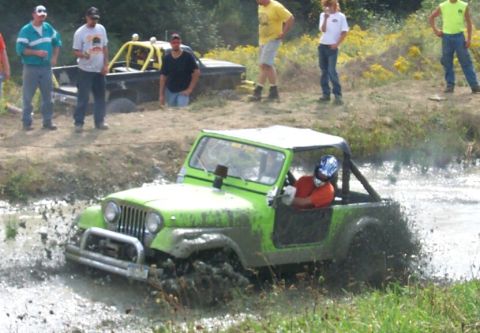 1979 Ford F-150 - A green jeep navigates a muddy track while spectators observe the off-road event.