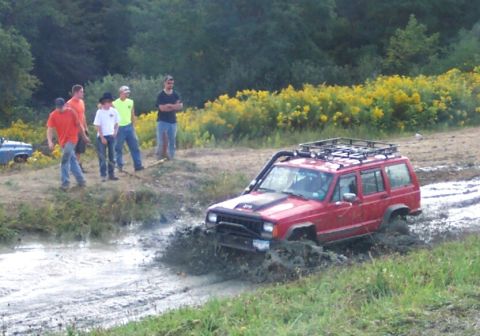 1979 Ford F-150 - A red Jeep Cherokee XJ navigates a muddy trail, kicking up water and mud.