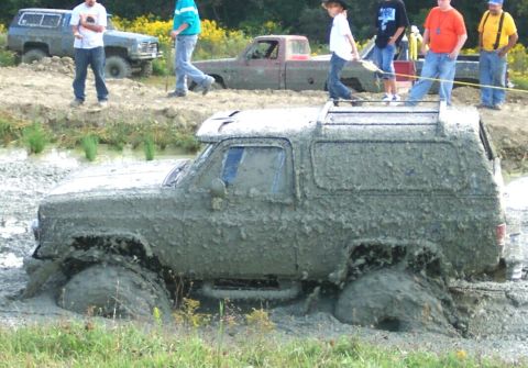 1979 Ford F-150 - A heavily mud-covered SUV is stuck in a muddy area, with several people observing the scene.
