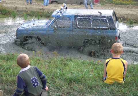 1979 Ford F-150 - A blue SUV is stuck in a mud pit, with two young boys observing the scene.