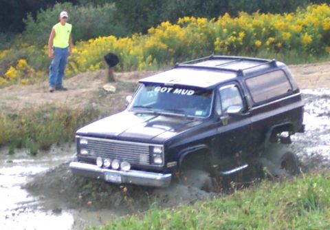 1979 Ford F-150 - A person watches as a black SUV navigates through a muddy terrain, with yellow flowers in the background.