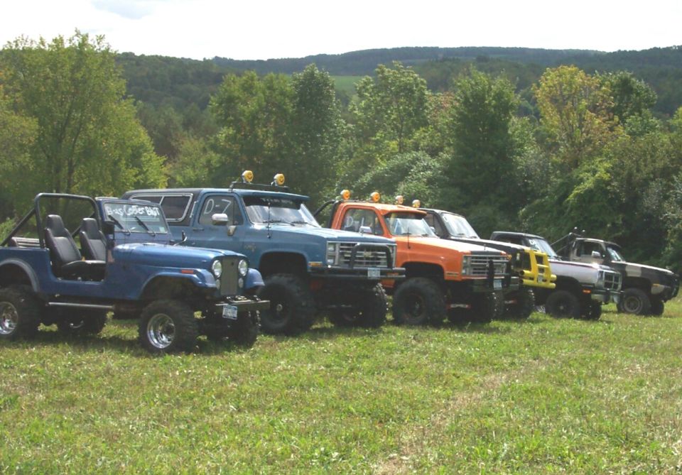 Line of lifted off-road trucks parked on grass, including a blue Jeep and several pickup trucks