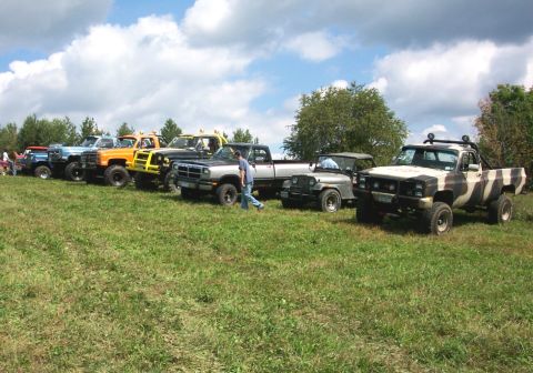 1979 Ford F-150 - Several off-road vehicles, including trucks and Jeeps, are lined up on a grassy incline under a partly cloudy sky.