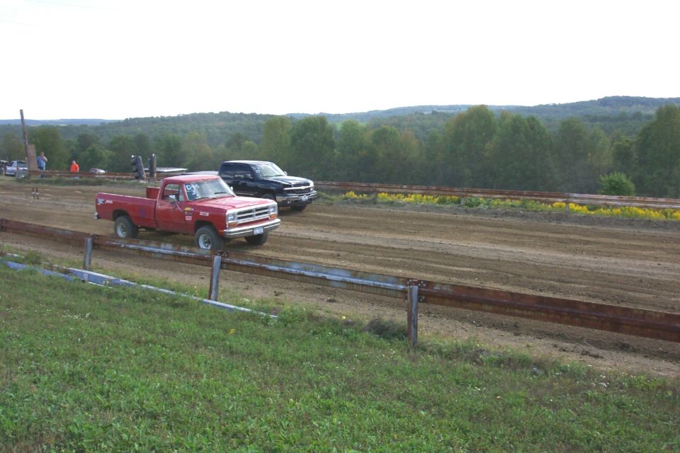 1979 Dodge pickup truck racing a black SUV on a dirt track