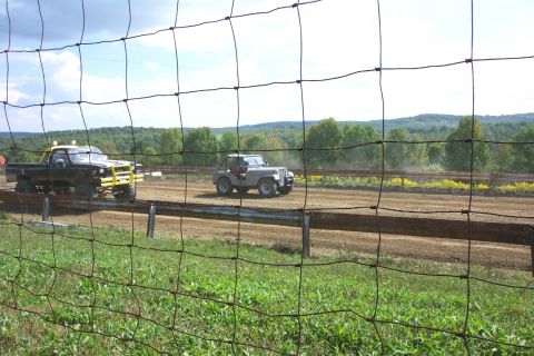 1979 Ford F-150 - Two vehicles compete on a dirt track, with trees and hills in the background.