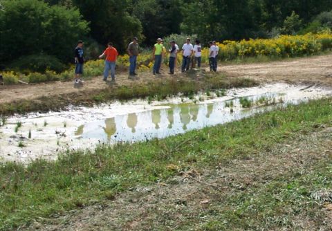1979 Ford F-150 - Several people stand on the bank of a muddy ditch, their reflections visible in the water.