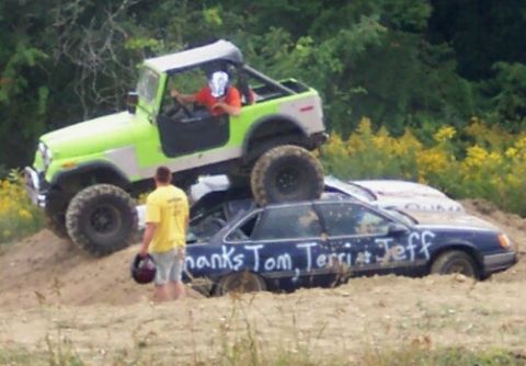 1979 Ford F-150 - A green off-road vehicle is positioned on top of a dark sedan in a muddy outdoor scene.