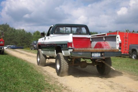 1979 Ford F-150 - Lifted pickup truck with a flatbed drives on a dirt road, kicking up dust. Another vehicle is visible in the background.