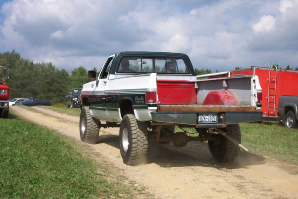 Rear view of lifted white and green pickup truck with flatbed, license plate RZK-2105