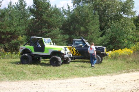 1979 Ford F-150 - Two modified off-road vehicles are parked on a grassy area with trees in the background.