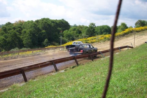 1979 Ford F-150 - Two pickup trucks compete on a dusty dirt track, with one kicking up a cloud of dust as it moves.