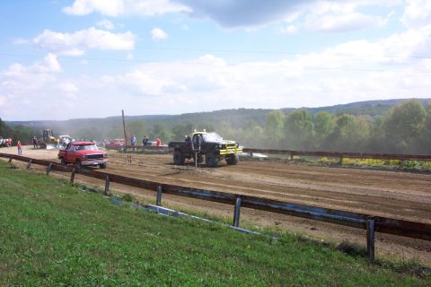 1979 Ford F-150 - Trucks race on a dirt track during an event with spectators watching.