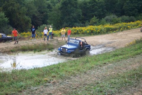 1979 Ford F-150 - A blue Jeep CJ-7 navigates a muddy track while onlookers observe the off-road activity.