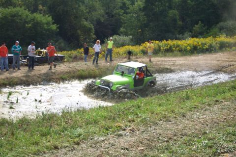 1979 Ford F-150 - A bright green Jeep navigates a muddy track during an off-road event, with onlookers observing the action.