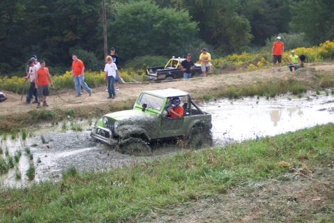 1979 Ford F-150 - A green Jeep navigates a muddy track with spectators and another vehicle nearby.